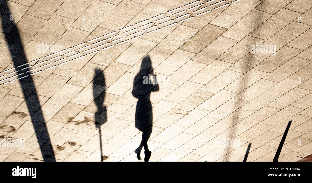 Indicatori tattili per pavimentazione e silhouette d'ombra di una giovane donna che cammina da sola sulla piazza della città in seppia bianco e nero Foto Stock