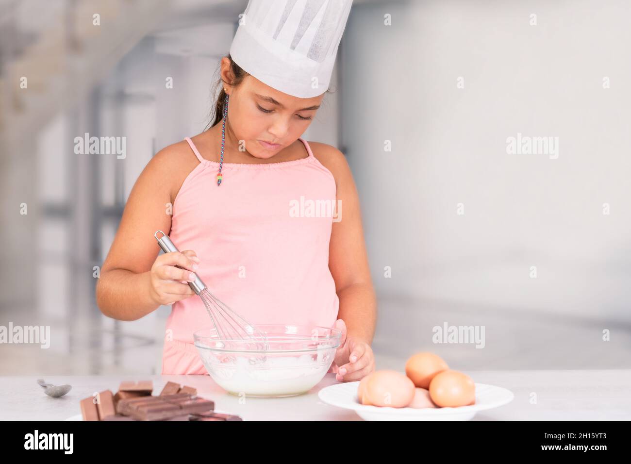 Ragazza latino-americana in cappello di uno chef preparare una torta al cioccolato Foto Stock