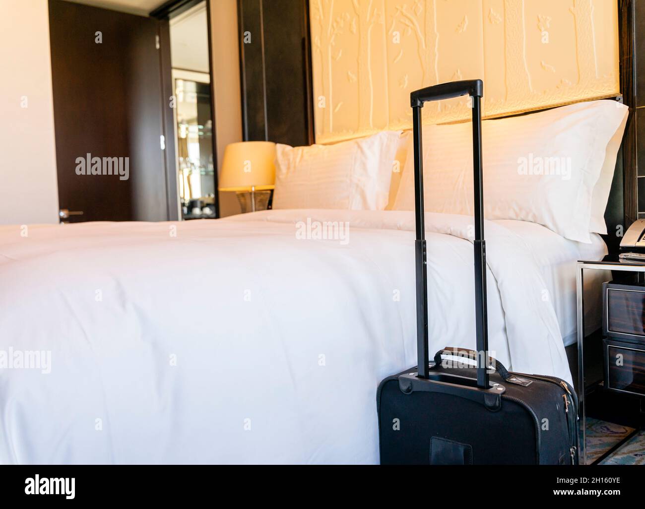Valigia bagagli accanto al letto king-size appena fatto in una suite da camera d'hotel Foto Stock