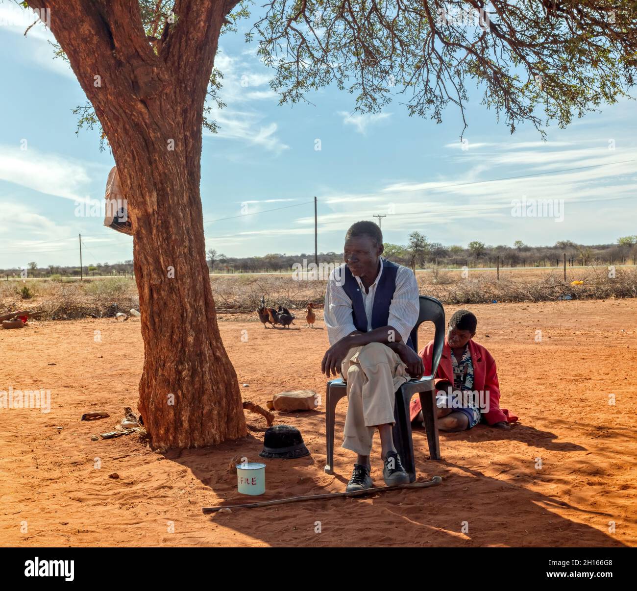 Vecchio africano in un villaggio in Botswana seduto di fronte al cortile nella sporcizia, con la figlia giorno di sole, Foto Stock