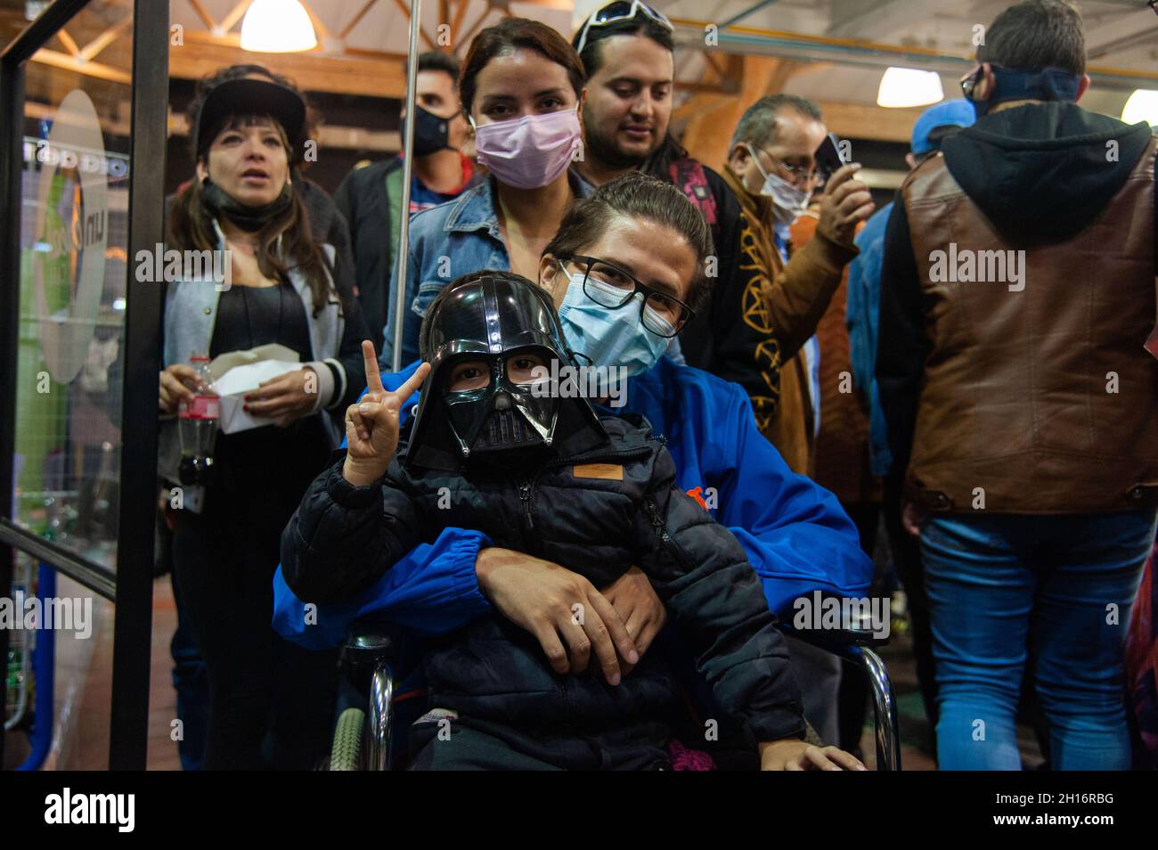 Un padre su una sedia a rotelle porta suo figlio sulle braccia indossando una maschera personaggio Star Wars Darth Vader durante il primo giorno del DIVANO (Salon del Ocio y la Fantasia) 2021, una fiera rivolta al pubblico geek in Colombia che mescola Cosplay, gioco, Supereroi e appassionati di film provenienti da tutta la Colombia, a Bogotà, Colombia, il 14 ottobre 2021. Foto Stock