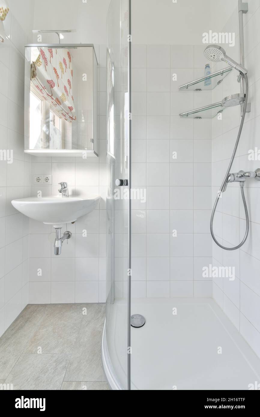 Cabina doccia e lavandino in ceramica sotto il mobile a specchio appeso su  una parete piastrellata bianca in un bagno minimalista alla luce del sole  Foto stock - Alamy