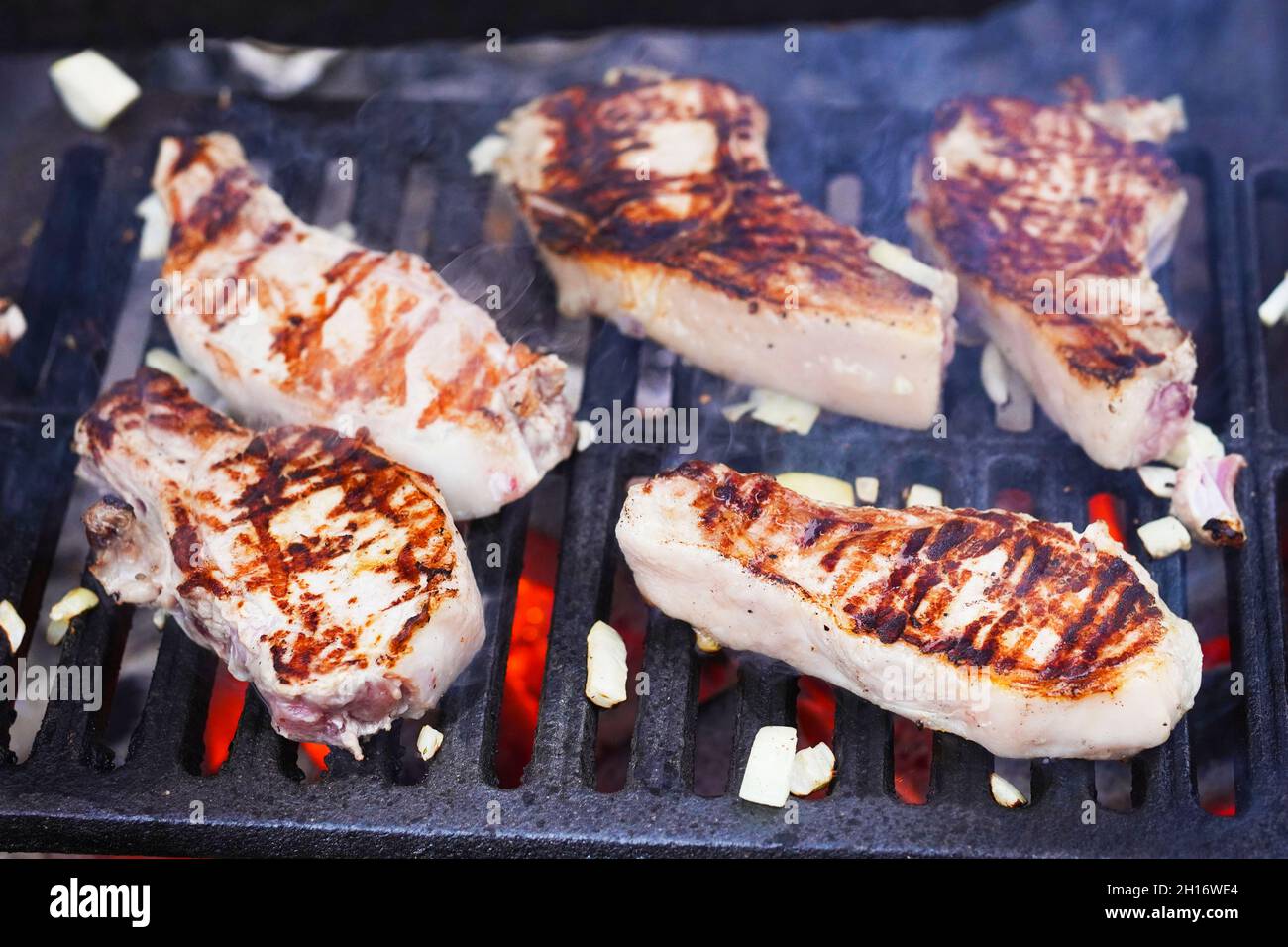 Barbecue Grill Pit con incandescente e fiammeggiante caldo, bistecche crude e cipolla, cibo di fondo, primo piano. Messa a fuoco selettiva. Foto Stock