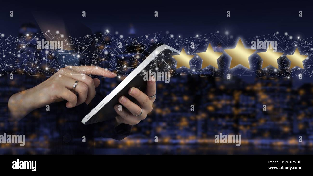 Mano touch tablet bianco con ologramma digitale cinque stelle segno sulla città scuro sfondo sfocato. Aumentare la valutazione o la classificazione, la valutazione e la classificazione Foto Stock