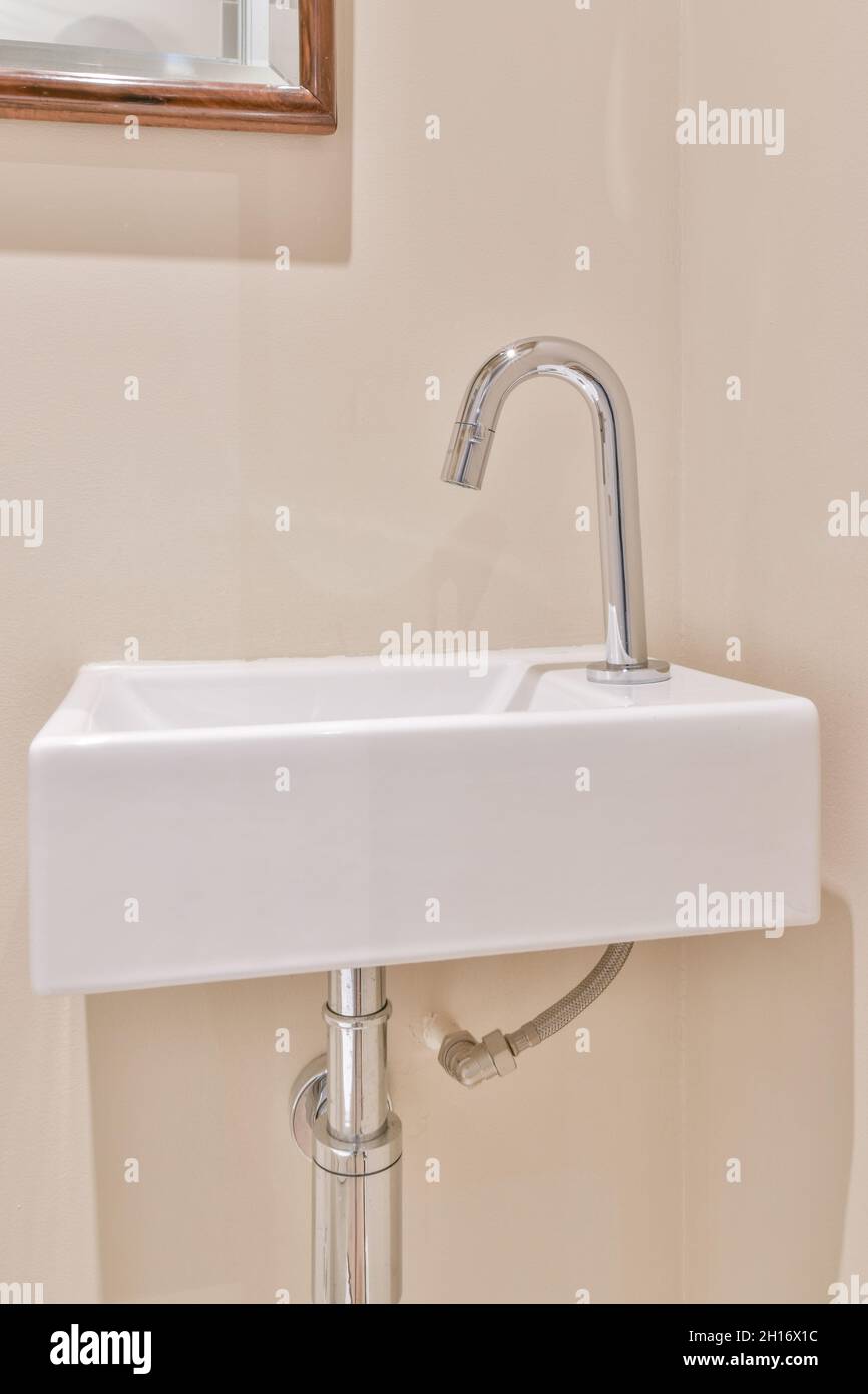 Lavello in ceramica bianca con rubinetto cromato lucido installato su parete beige in bagno Foto Stock