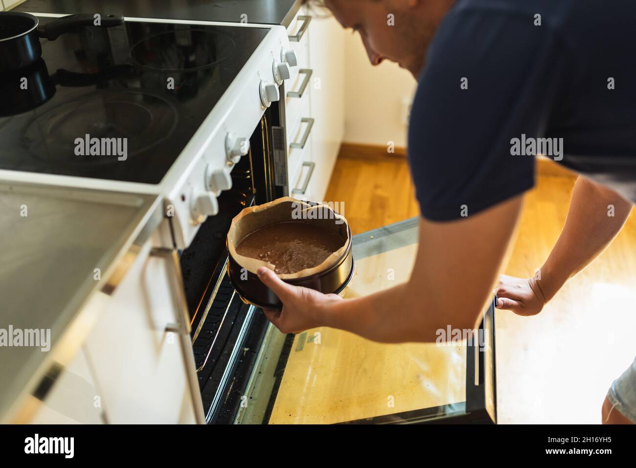 Da sopra vista laterale del fornello maschio adulto in cucina luce che apre  la porta del forno e che mette la forma di cottura riempita con la pastella  della torta di cioccolato