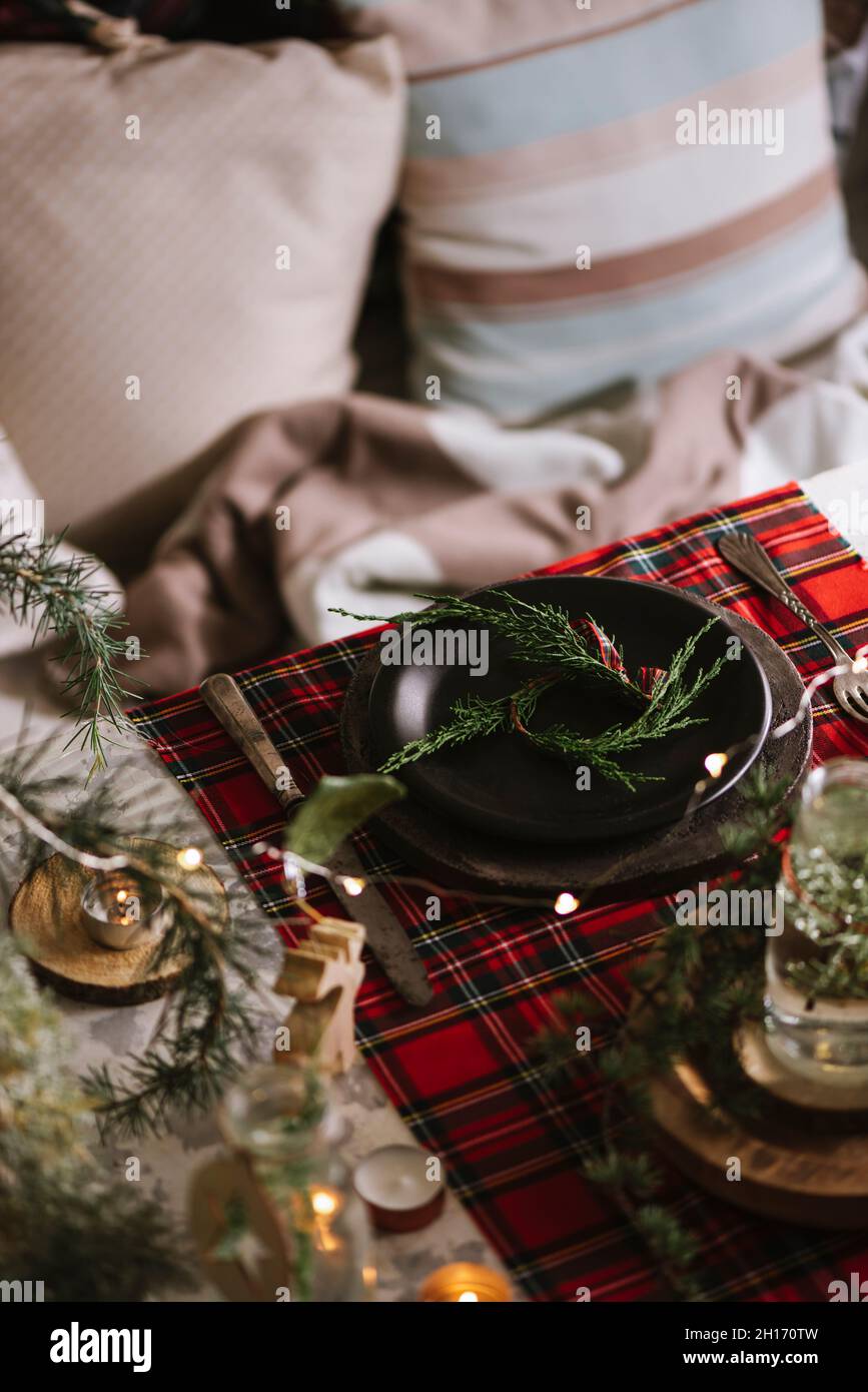 Da sopra tavolo di Natale con corona su piatto di ceramica su tovaglia a scacchi rosso sullo sfondo Foto Stock