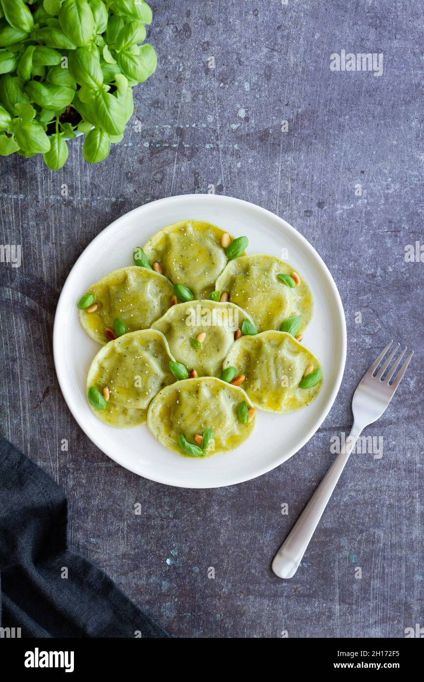 Vista dall'alto di gustosi ravioli con basilico decorato con pinoli serviti su piatto rotondo bianco su tavolo in cucina luminosa Foto Stock