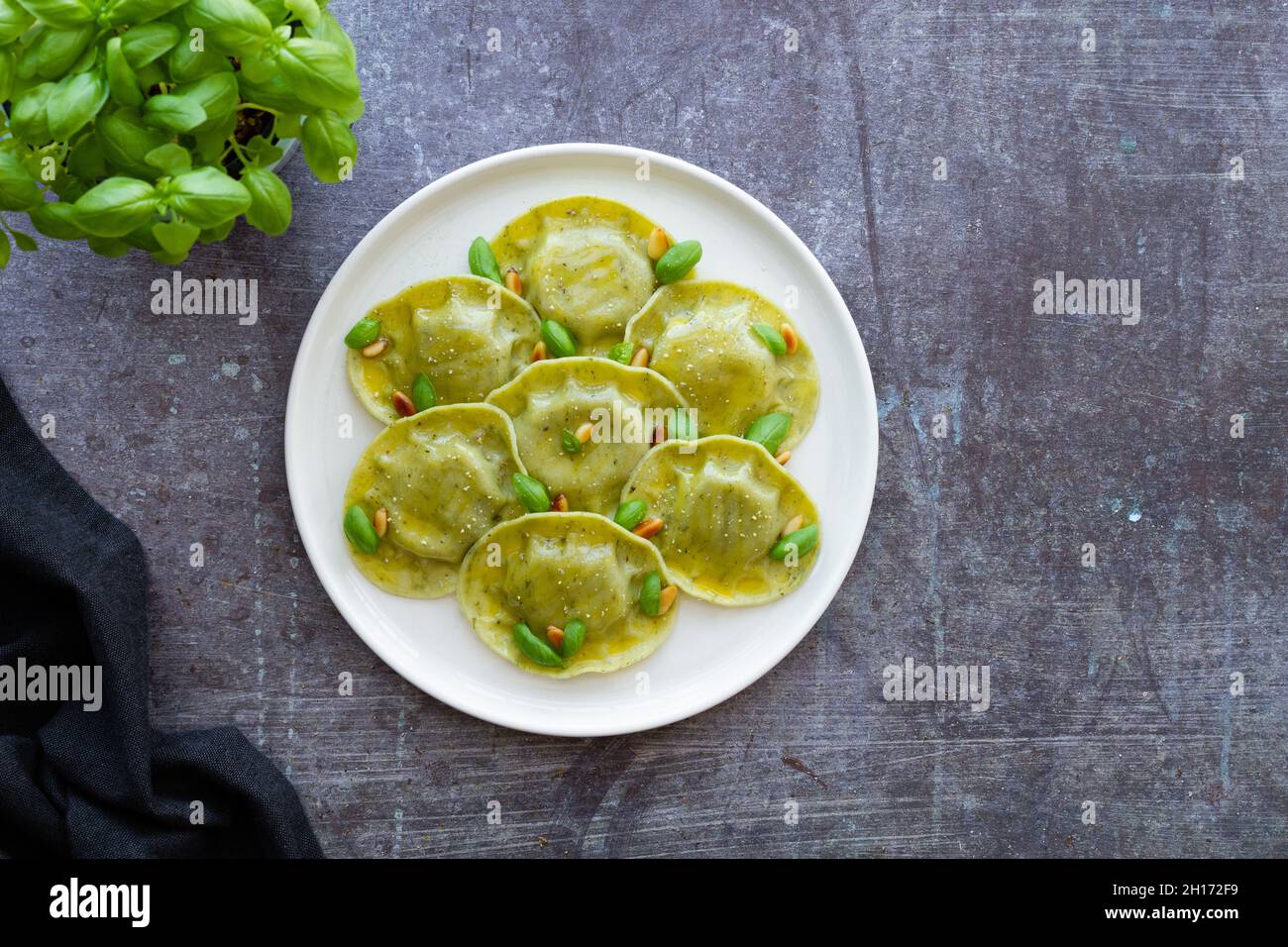 Vista dall'alto di gustosi ravioli con basilico decorato con pinoli serviti su piatto rotondo bianco su tavolo in cucina luminosa Foto Stock