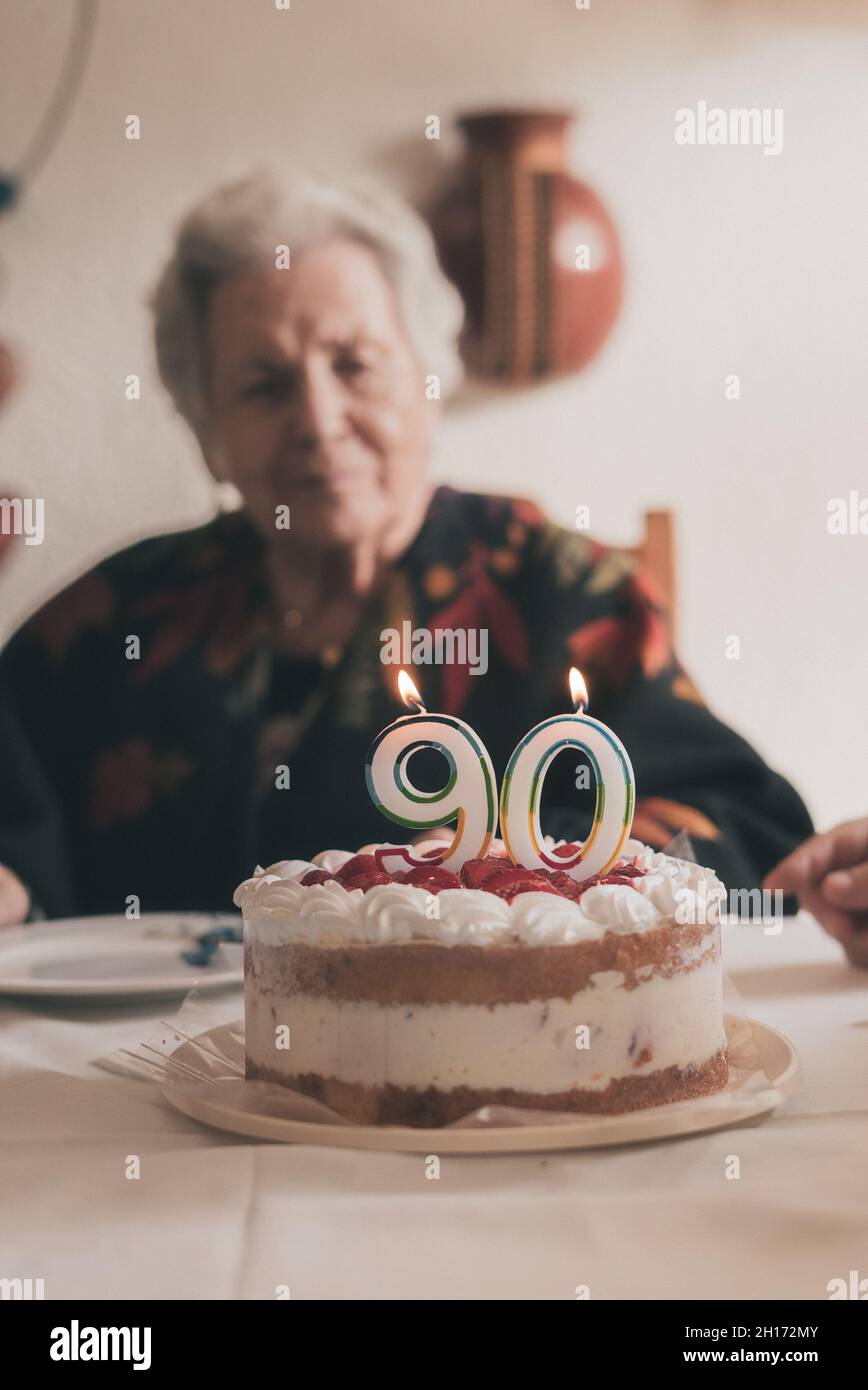 Donna anziano che soffia le candele sulla torta di compleanno allora che batte le mani mentre festeggia 90th anniversario con il parente nel paese Foto Stock