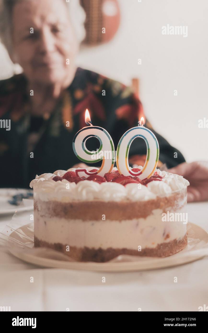 Donna anziano che soffia le candele sulla torta di compleanno allora che batte le mani mentre festeggia 90th anniversario con il parente nel paese Foto Stock