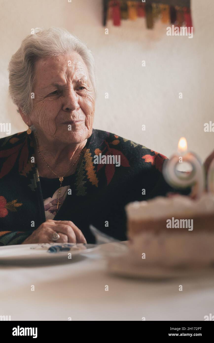 Donna anziano che soffia le candele sulla torta di compleanno allora che batte le mani mentre festeggia 90th anniversario con il parente nel paese Foto Stock