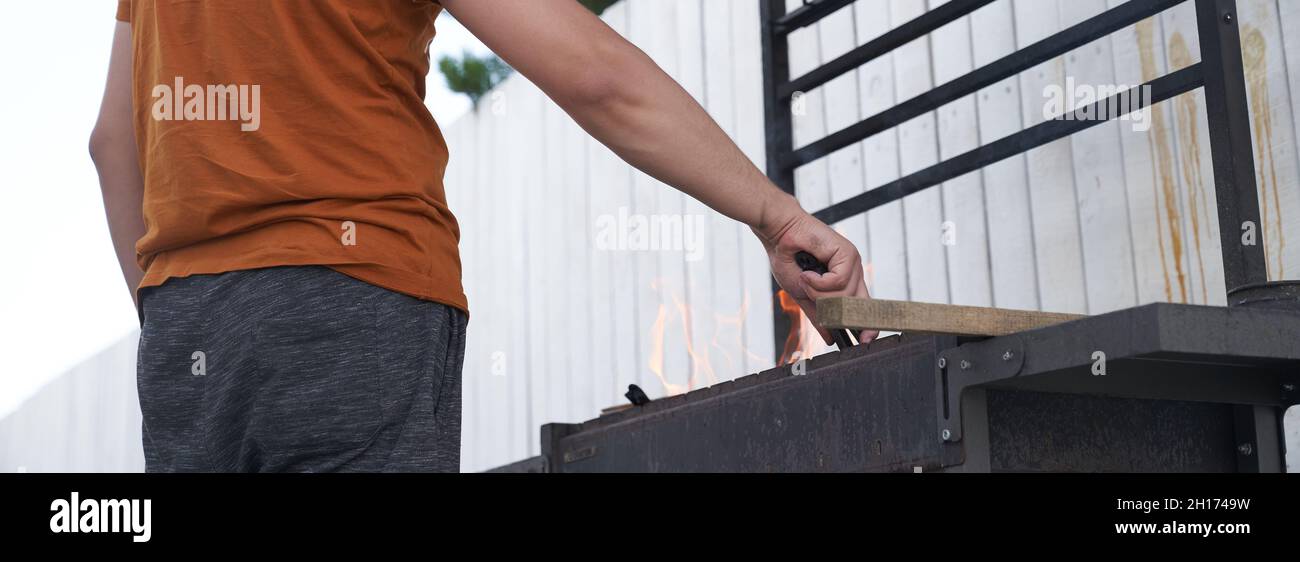 Una mano dell'uomo tiene una griglia quadrata del barbecue, sopra il fuoco. Il concetto di preparazione per un barbecue. Foto di alta qualità Foto Stock