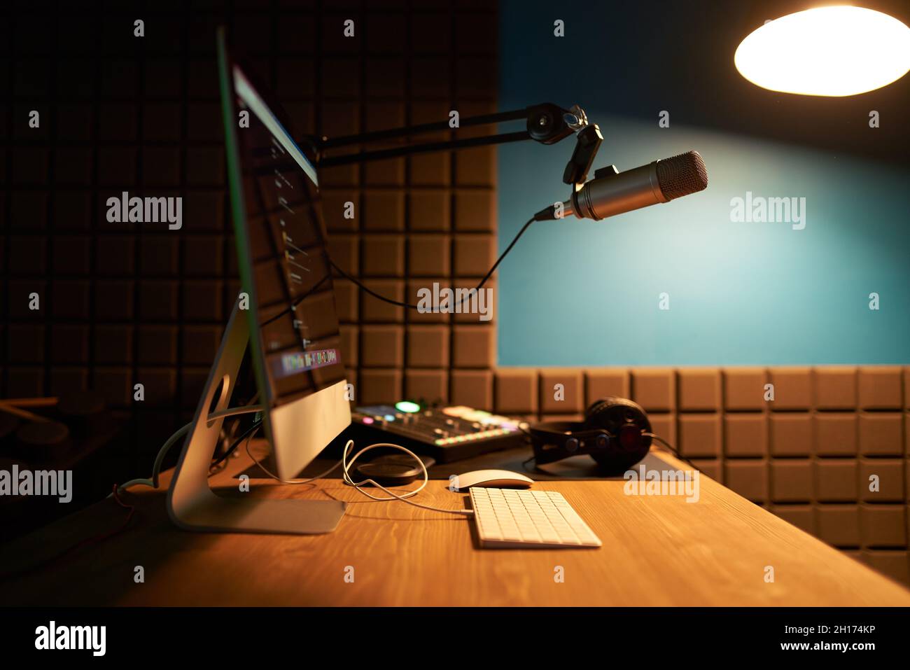 Computer e tastiera moderni posti su un tavolo di legno con microfono su treppiede e cuffie in studio di registrazione podcast scuro Foto Stock