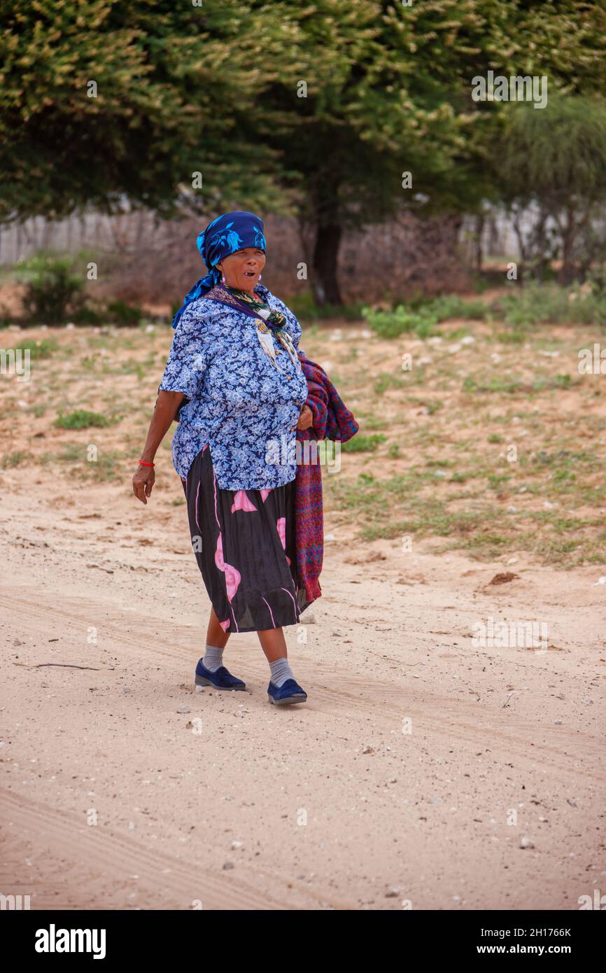 Vecchia donna bushman da Kalahari centrale, villaggio New Xade in Botswana, a piedi su una strada sterrata Foto Stock