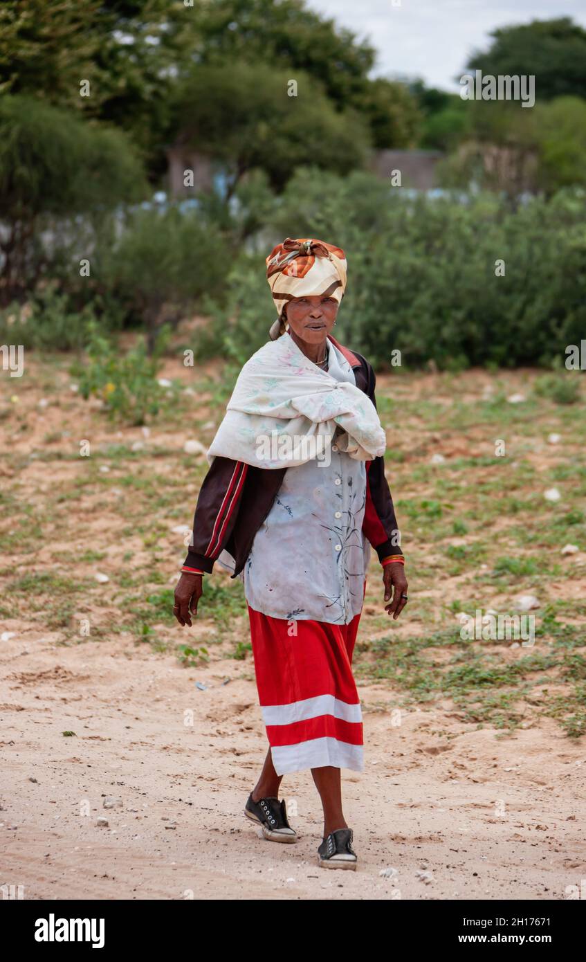 Vecchia donna bushman da Kalahari centrale, villaggio New Xade in Botswana, a piedi su una strada sterrata Foto Stock