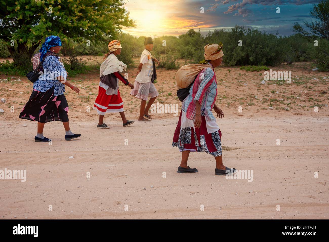 Gruppo di quattro donne boscimane di Kalahari centrale, villaggio New Xade in Botswana, a piedi su una strada sterrata Foto Stock