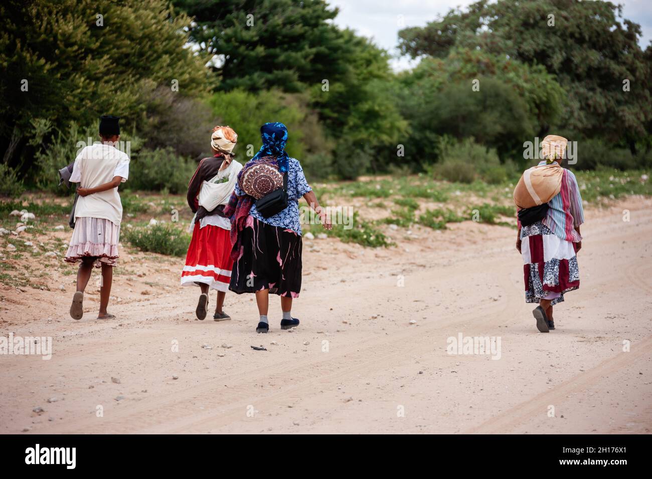 Gruppo di quattro donne boscimane di Kalahari centrale, villaggio New Xade in Botswana, a piedi su una strada sterrata Foto Stock