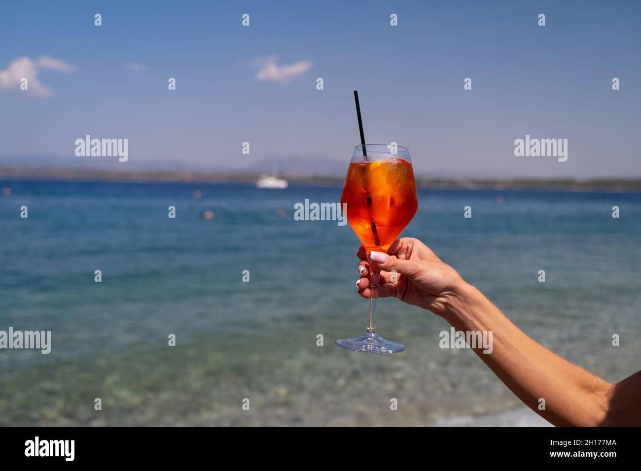 Donna mano che tiene un bicchiere di cocktail Aperol Spritz su sfondo marino Foto Stock