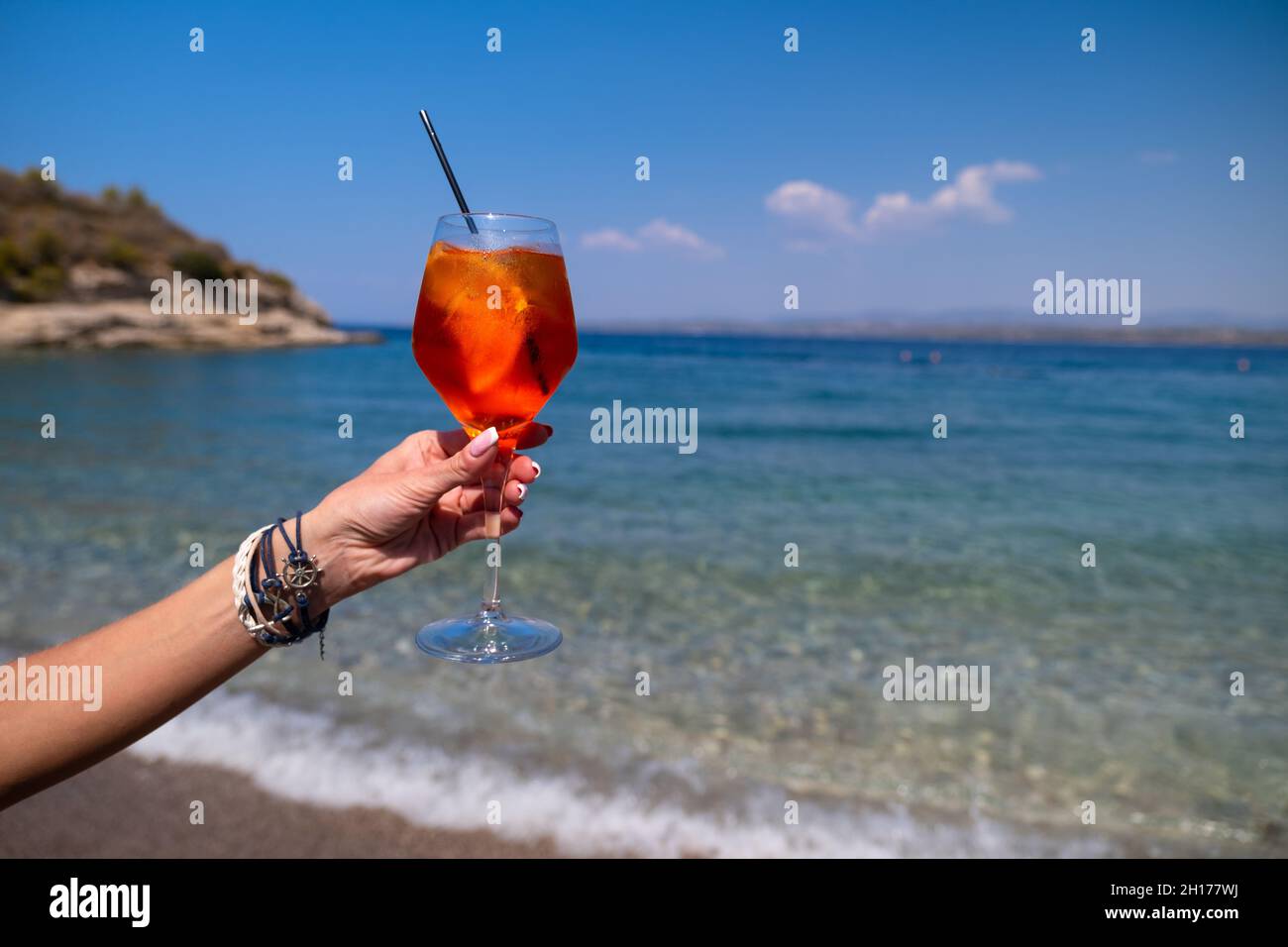 Donna mano che tiene un bicchiere di cocktail Aperol Spritz su sfondo marino Foto Stock
