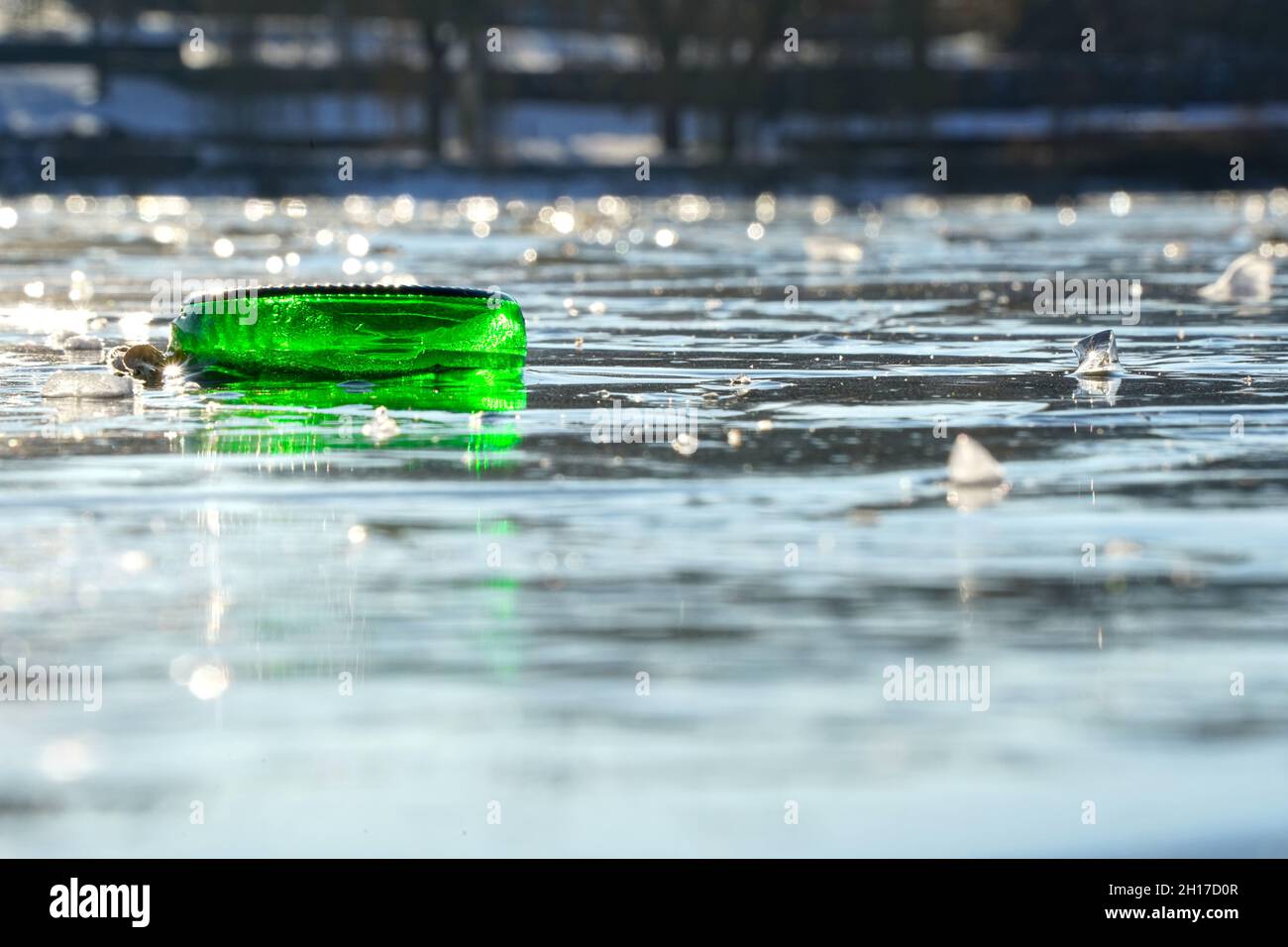 Il fondo della bottiglia verde è congelato solido nel lago. Piccole schegge di ghiaccio creano riflessi sulla superficie dell'acqua. Parte di un flacone. Vi. Anteriore Foto Stock