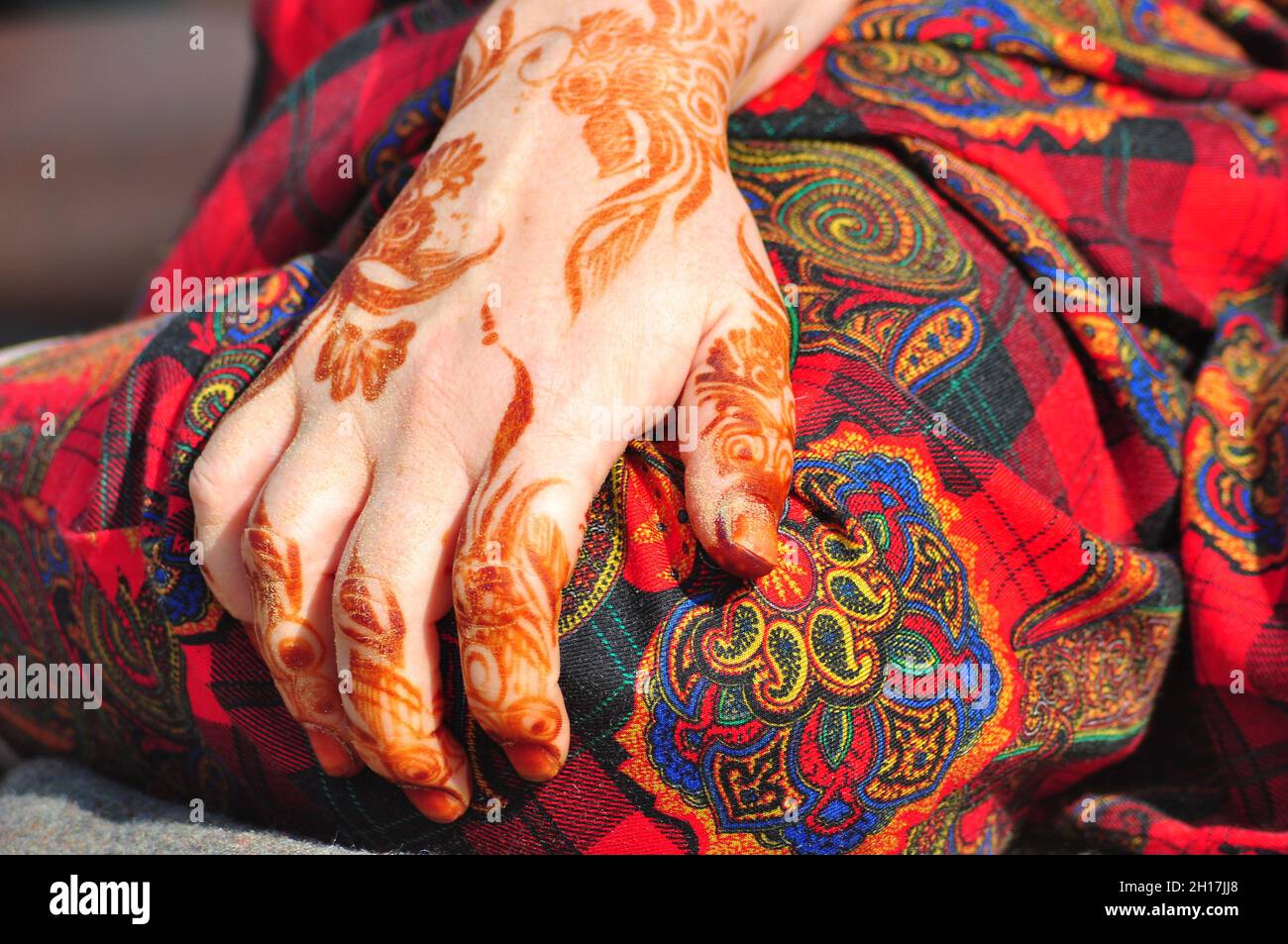 Una donna “expat” (espatriata) siede sulla sabbia del deserto vicino ad al-Ain negli Emirati Arabi Uniti con i suoi amici, dopo aver giocato nella sabbia mette la mano sul ginocchio. Questa donna è negli Emirati Arabi Uniti per lavorare come insegnante di scuola, la popolazione expat negli Emirati Arabi Uniti supera il numero dei cittadini da quasi 40 a 1.This donna ha Henna modelli disegnati sulla sua mano, questi segni sbiadiranno entro le prossime 3 settimane. Foto Stock