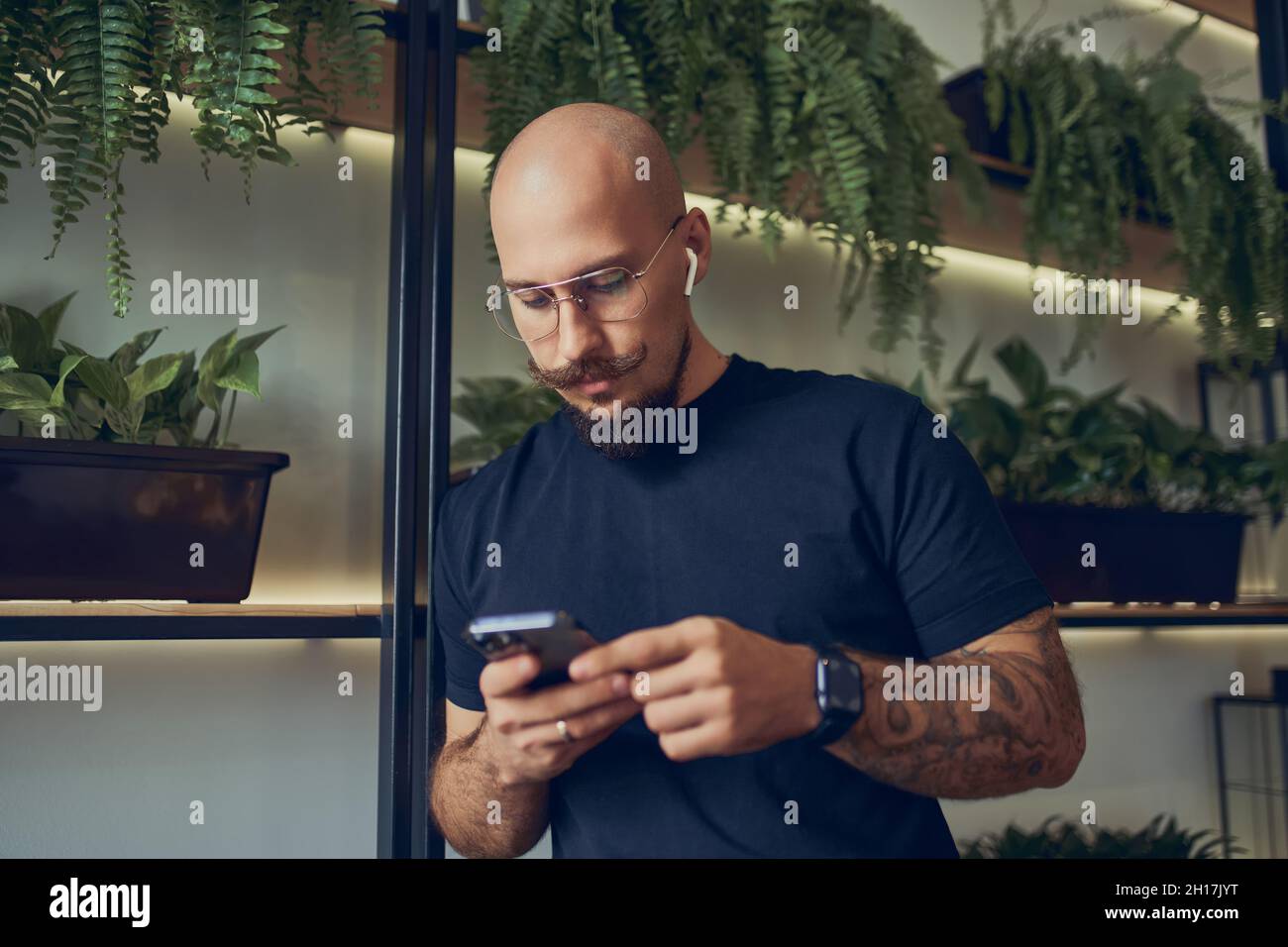 L'uomo d'affari concentrato utilizza lo smartphone con le cuffie mentre si trova in ufficio. Lavoro a distanza. Foto Stock