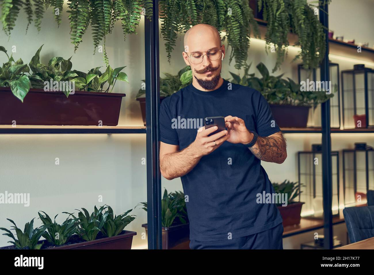 L'uomo d'affari concentrato utilizza lo smartphone con le cuffie mentre si trova in ufficio. Lavoro a distanza. Foto Stock