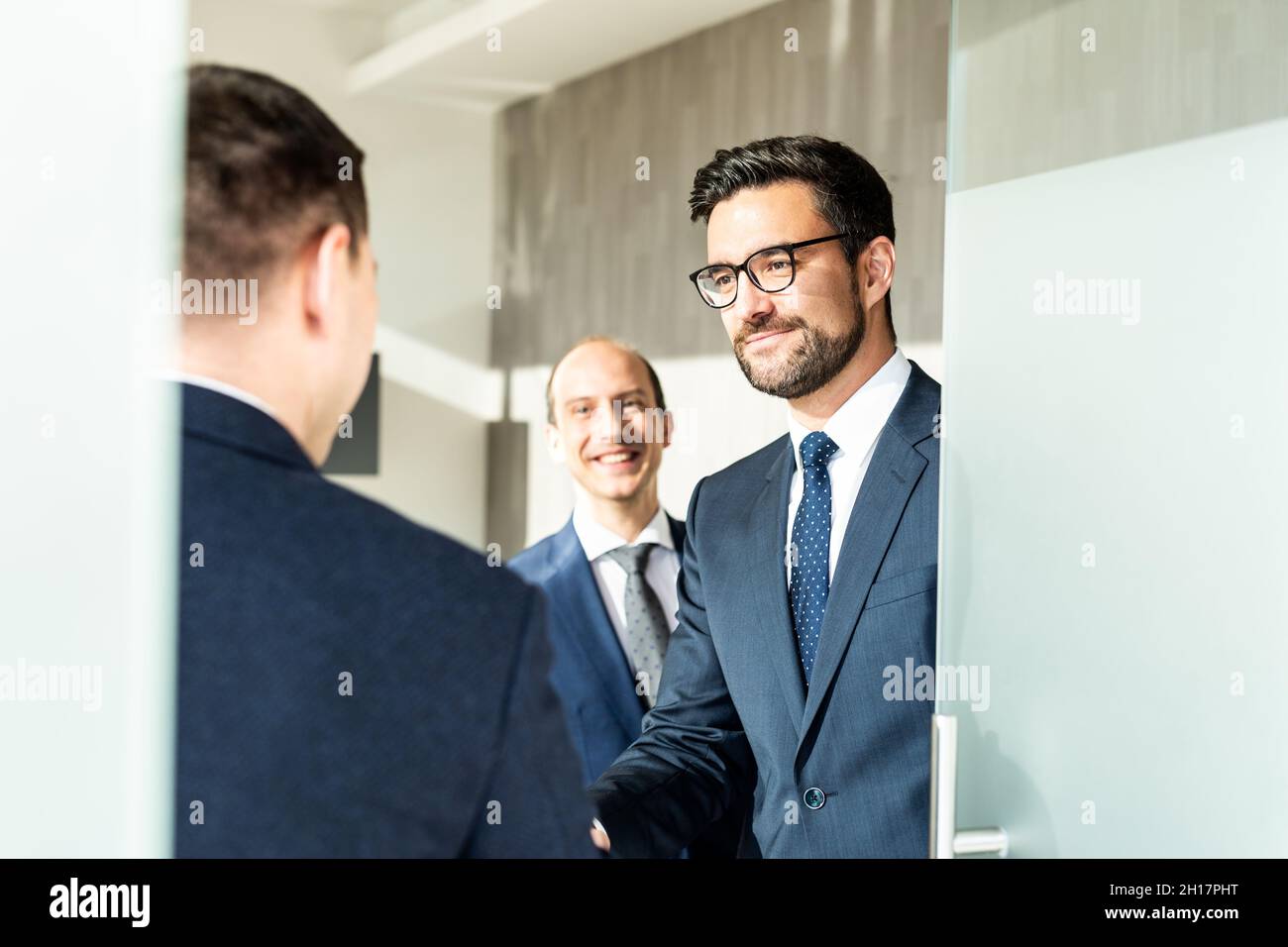 Gruppo di allegri uomini d'affari fiduciosi che salutano con una stretta di mano alla riunione d'affari in un ufficio moderno. Foto Stock