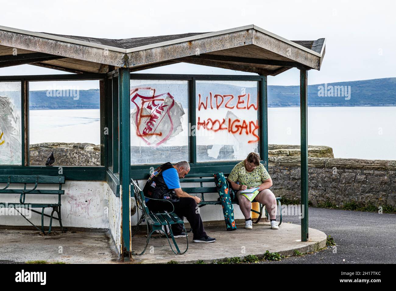 Due persone sedute in un rifugio lungo il mare, con finestre rotte e graffiti Foto Stock