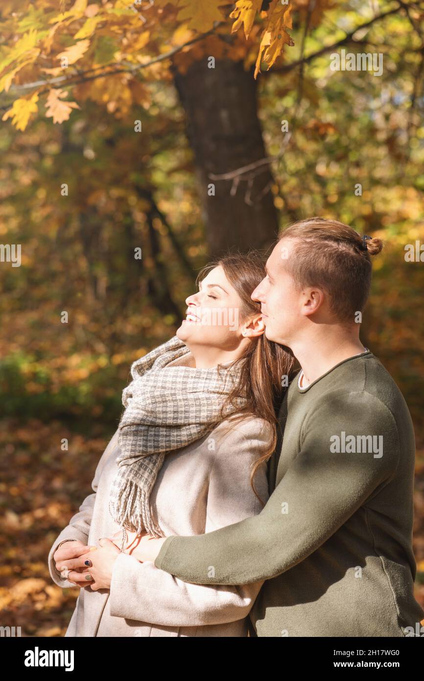 Tempo libero, rapporto, concetto di natura. L'uomo abbraccia la ragazza e gode di luce solare autunnale sotto l'albero di quercia con foglie gialle. Filtro luminoso per retroilluminazione. G Foto Stock