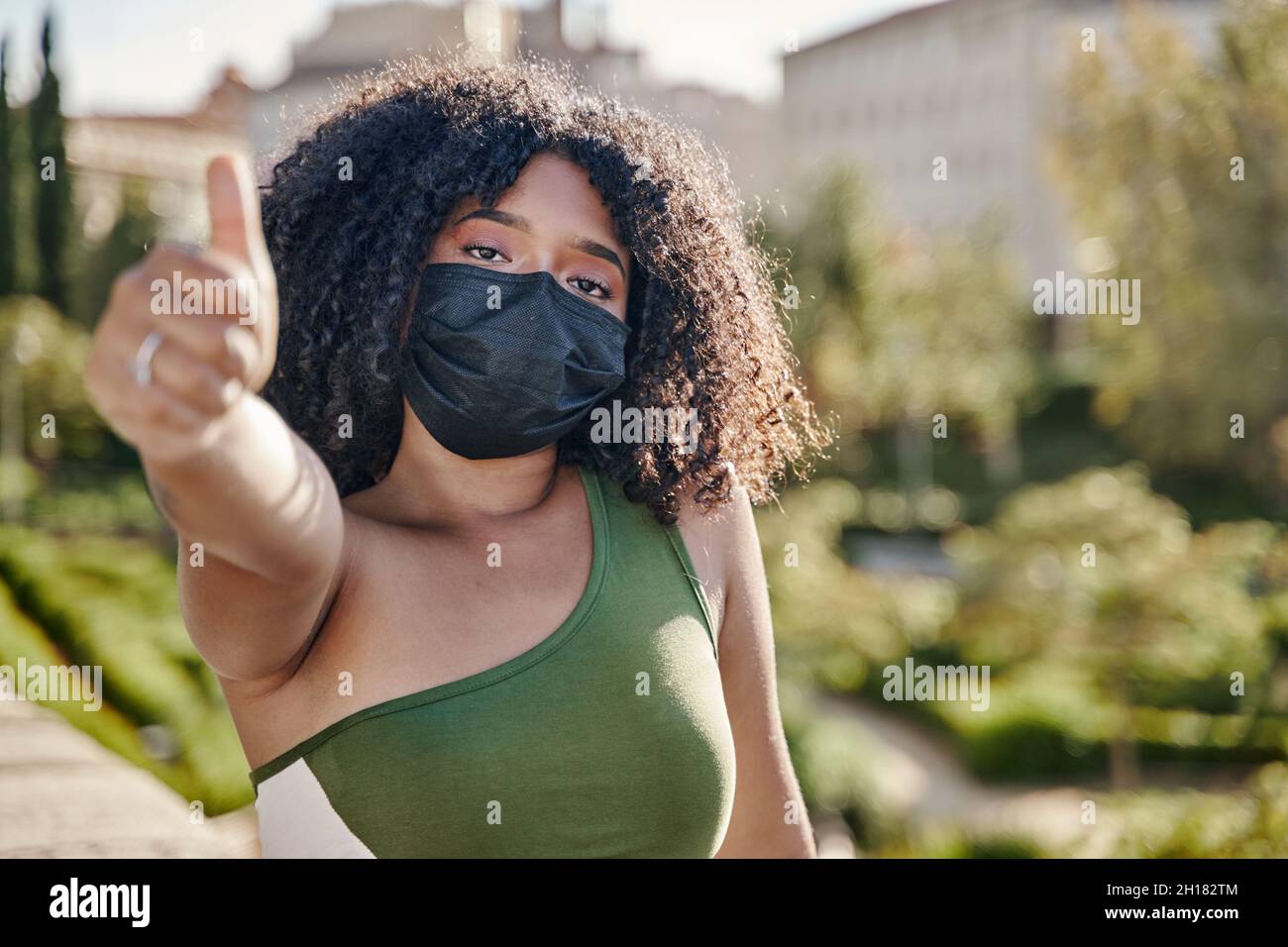 Ritratto allegro giovane donna latina in abiti casual e maschera sterile per il viso al sicuro da coronavirus covid-19 mostrando il pollice come gesto Foto Stock