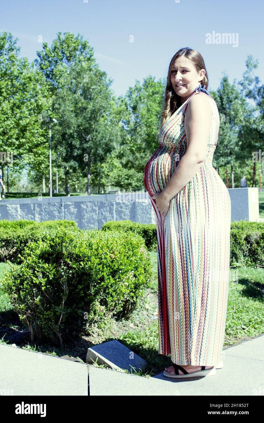 Donna incinta di sette mesi all'aperto in abito multicolore a righe. Scena del giorno Foto Stock