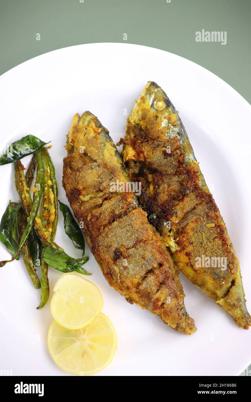 Sgombro indiano pesce fritto. Bangda Rava fritto. Pesce fritto intero servito su una foglia di banana con peperoncini fritti, fette di limone e spezie indiane. Foto Stock