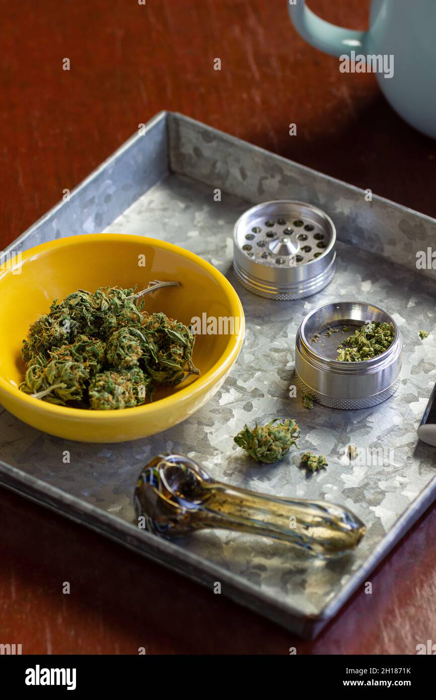 Germogli marijuana medici o fiori di canapa con macinacaffè di erbe e accessori per il fumo in vassoio di metallo con tazza di caffè Foto Stock