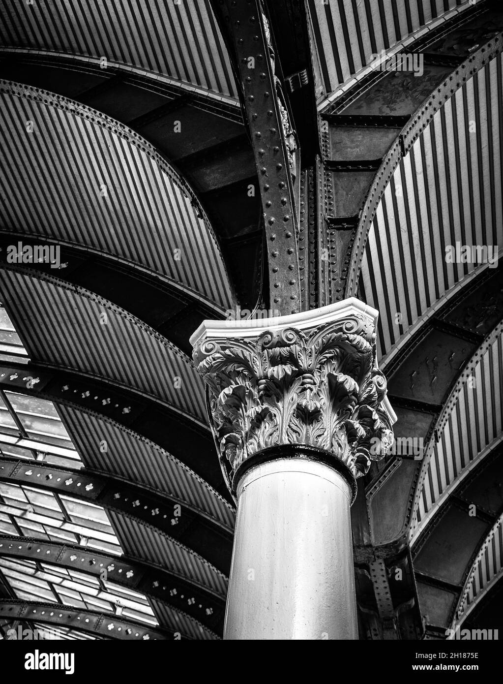 Vista verso l'alto di una storica colonna Corinzia del XIX secolo che sostiene un baldacchino. Un lucernario getta luce su un intricato ferro. Foto Stock