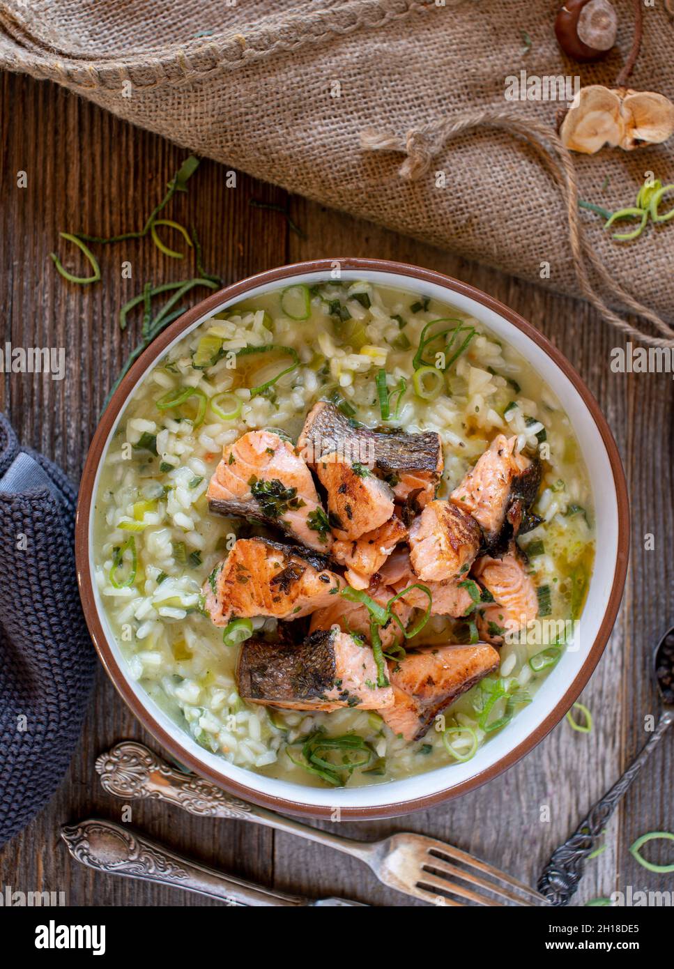 Filetto di salmone fritto con un delizioso risotto di porro servito in un recipiente rustico su un tavolo di legno. Vista dall'alto e immagine verticale Foto Stock