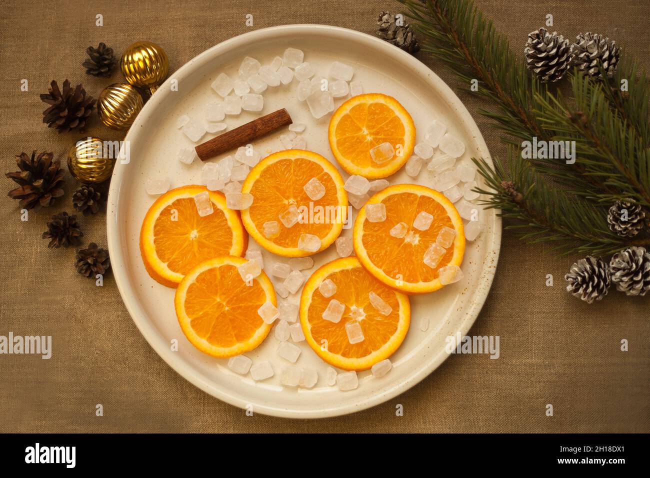 arance al piatto vicino albero di natale ramo, palle d'oro e coni di pino. Decorazioni tangerine Foto Stock