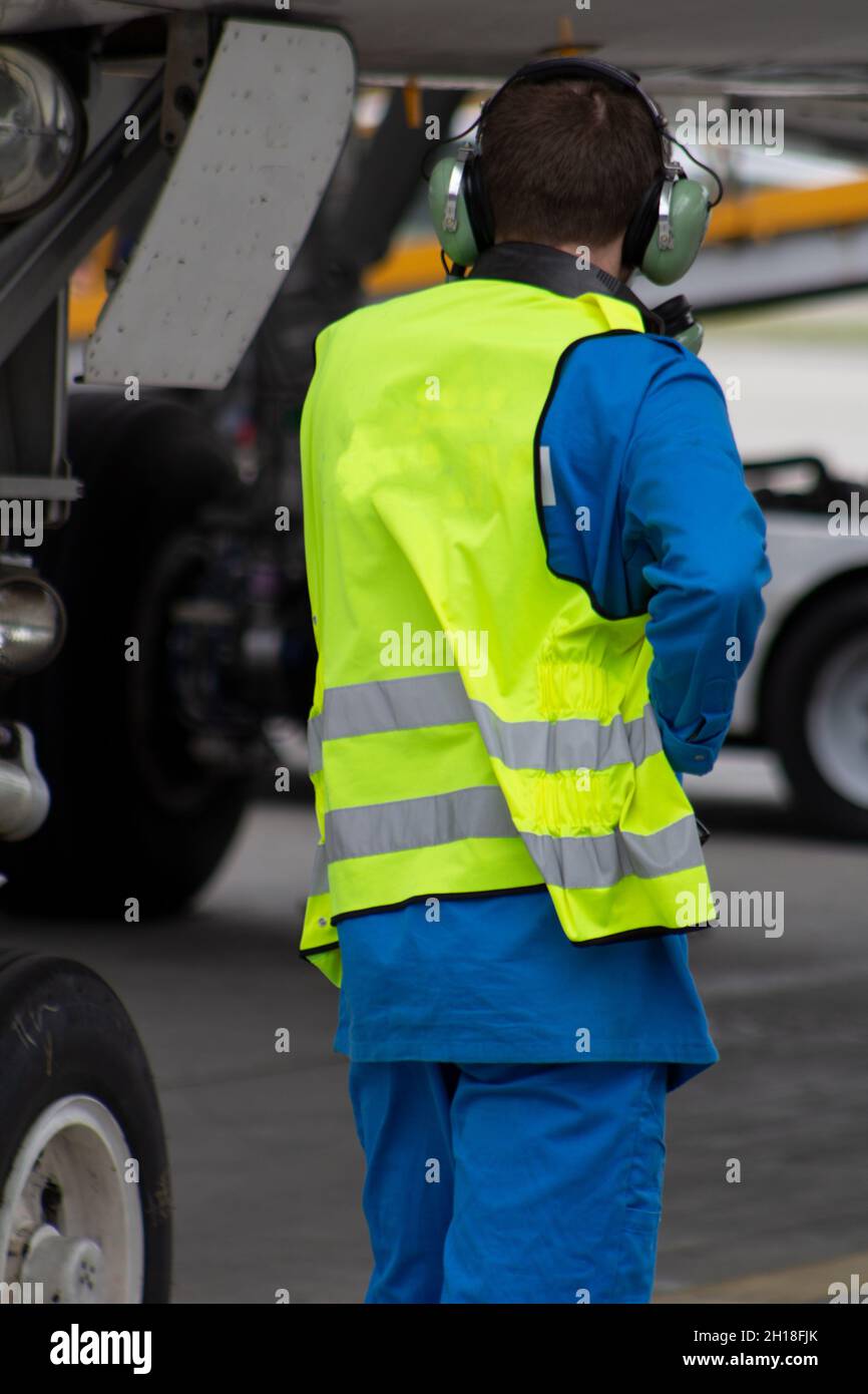Un uomo in un giubbotto riflettente. Un tecnico maschio si siede in una turbina e controlla il motore dell'aereo prima di volare. Manutenzione, riparazione dell'aviazione. Lavoratore aeroportuale Foto Stock