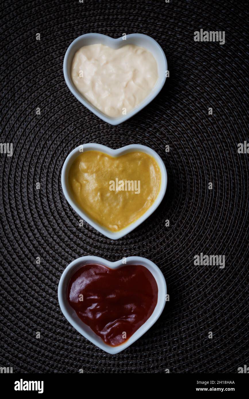 Ciotole a forma di cuore con ketchup, maionese e salsa di senape, colpo verticale. Foto Stock