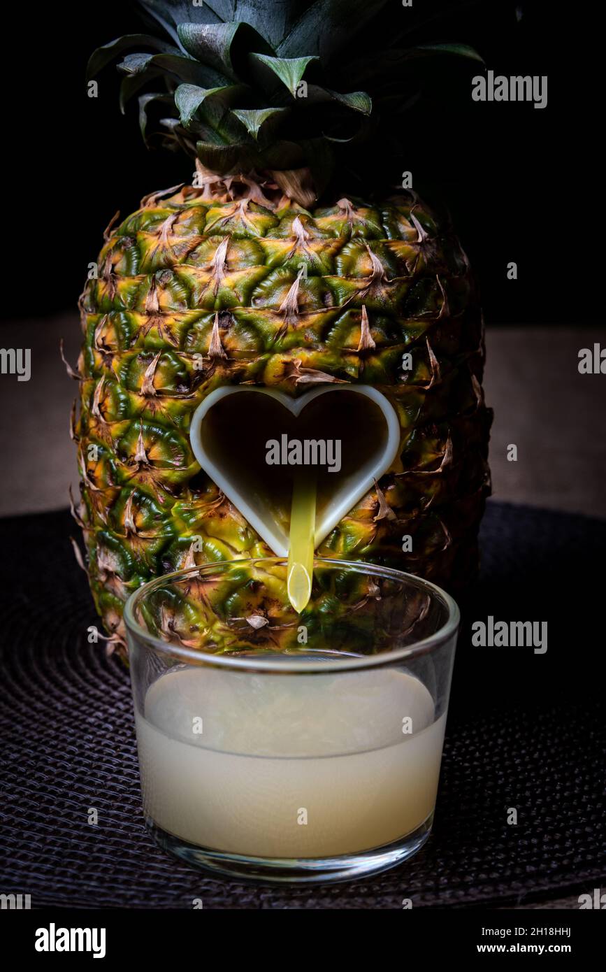 Ananas a cuore aperto al centro dal quale il succo scorre in un bicchiere. Foto Stock