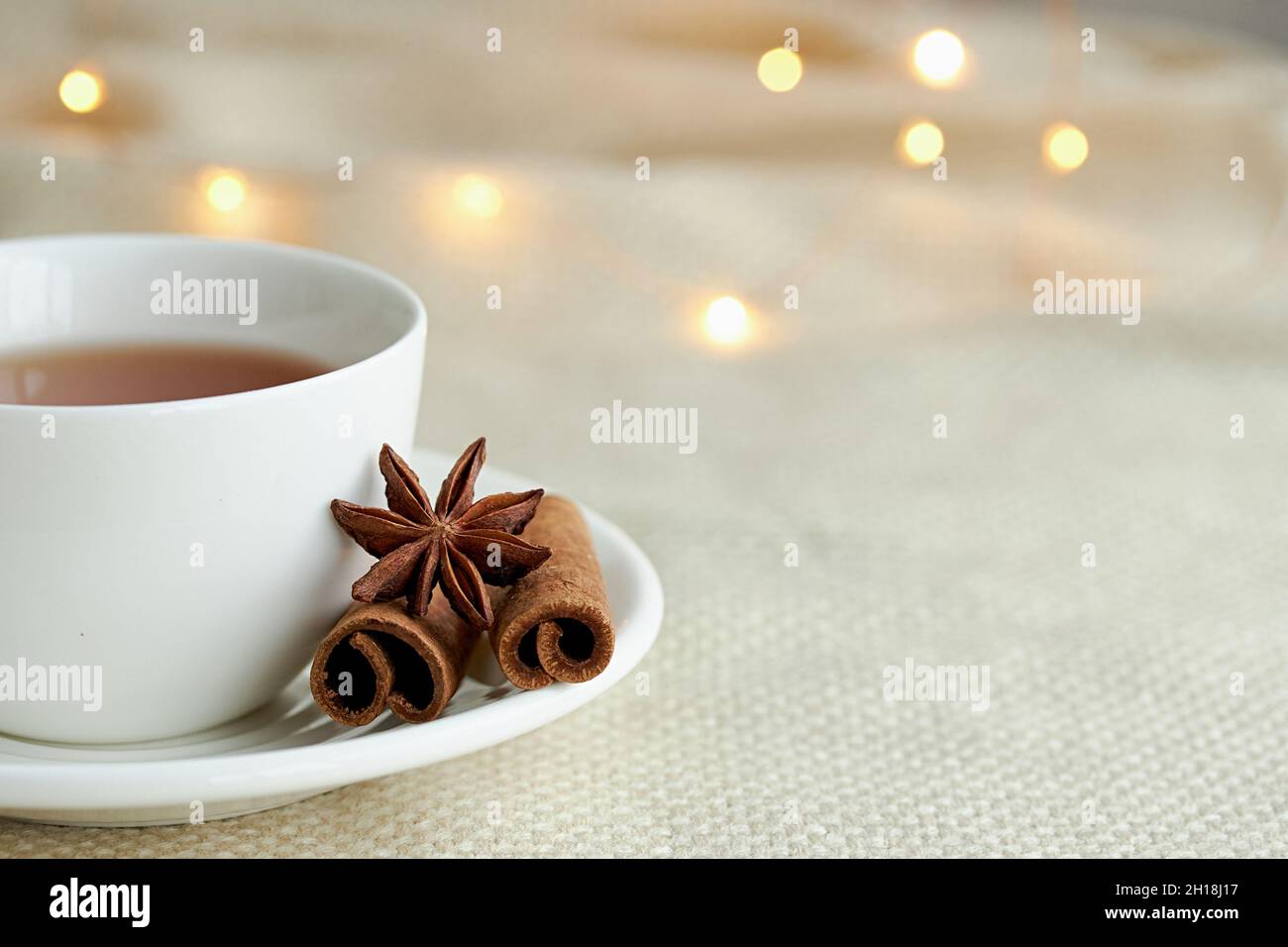 Tazza bianca di tè con cannella su quadri beige alle luci di Natale. Natale ancora vita. Foto Stock