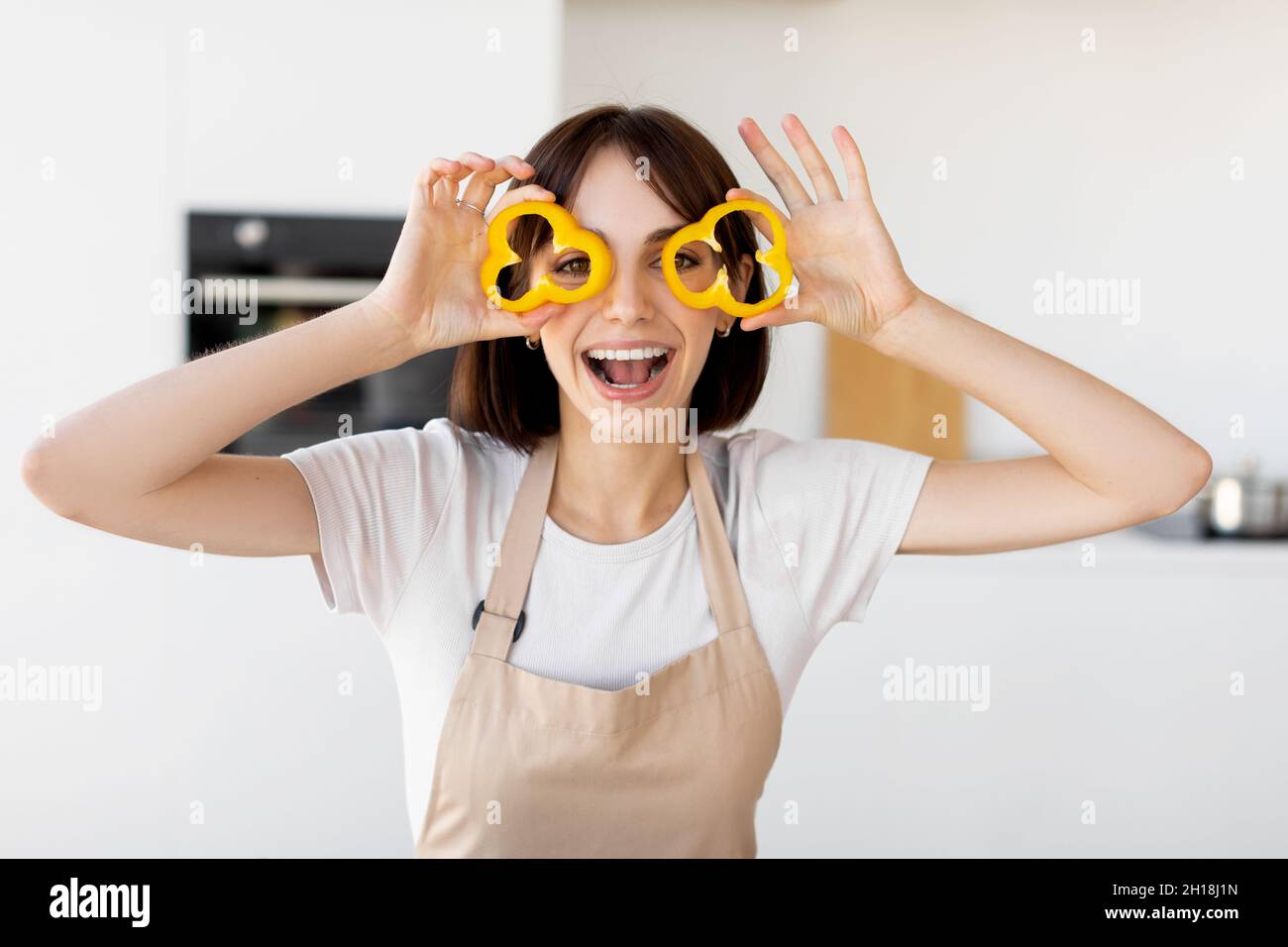 Signora giocosa che fa i bicchieri di peperone dolce, giocando con il cibo e imbrogliando intorno, cucinando l'insalata fresca in cucina Foto Stock