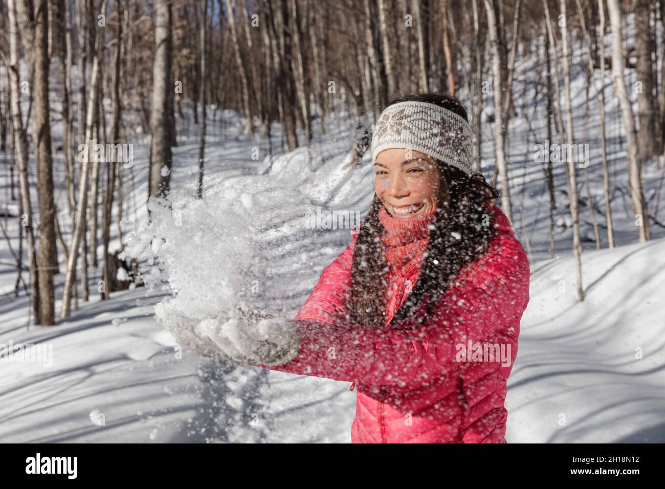 Inverno divertimento ragazza asiatica lancio neve fredda in aria giocando nella foresta. Stile di vita della stagione invernale Foto Stock
