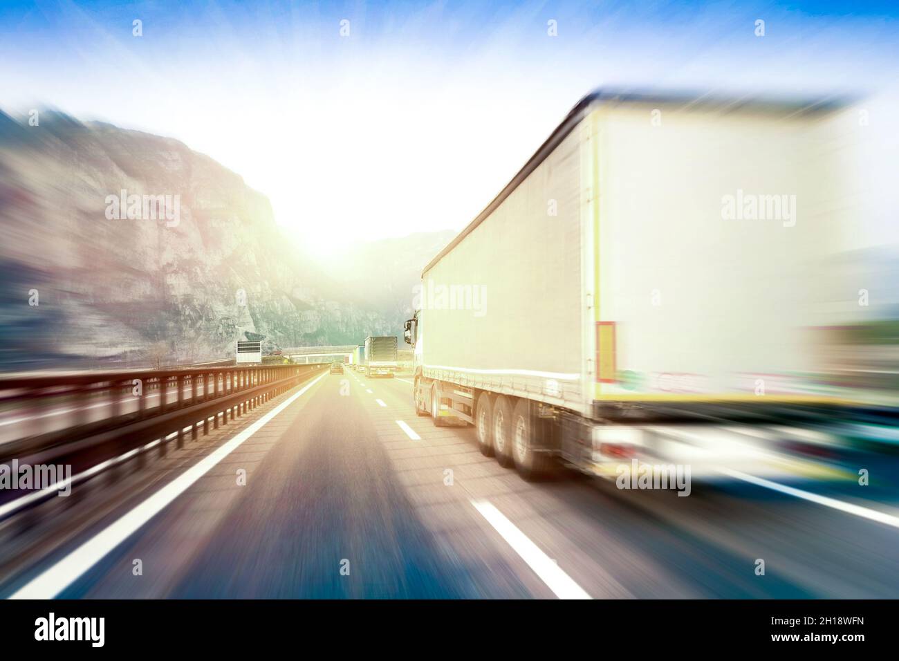 Semi-camion generici che accelera sull'autostrada al tramonto - concetto di industria di trasporto con contenitori di semitruck che guidano al passo di montagna Foto Stock