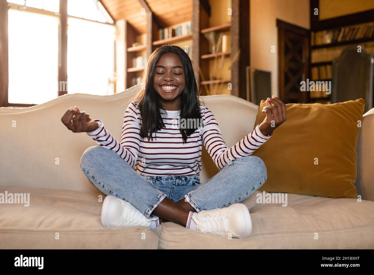 Gestione dello stress, benessere, consapevolezza. Calma giovane donna nera meditating con gli occhi chiusi sul divano a casa Foto Stock