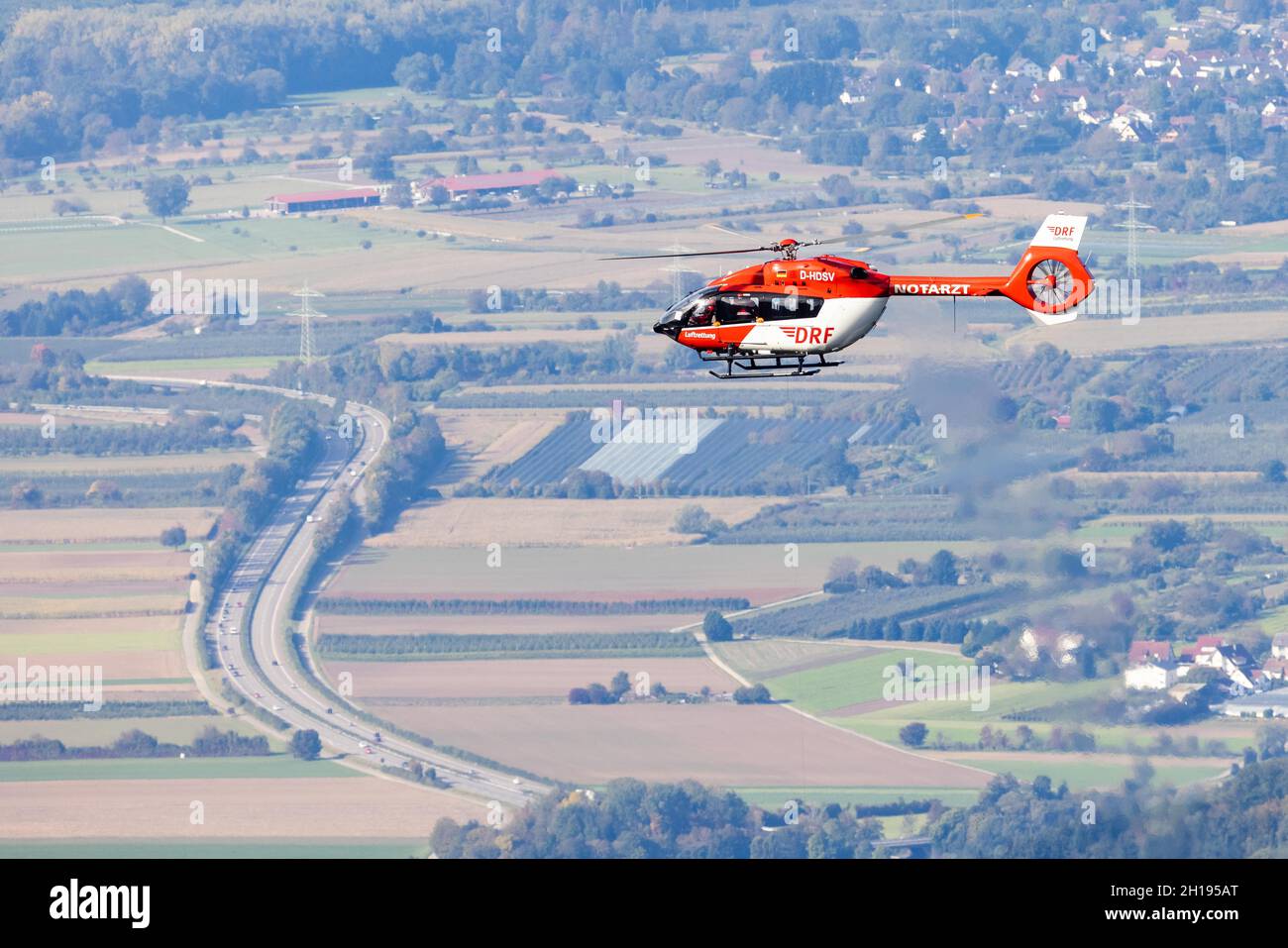 Waldkirch, Germania. 15 ottobre 2021. Un elicottero di soccorso della DRF Luftrettung vola in aria mentre un'autostrada federale a più corsie può essere vista sullo sfondo. Durante l'addestramento del verricello, l'equipaggio della stazione di Friburgo della DRF Luftrettung (cartello di chiamata Christoph 54) pratica le operazioni con il verricello sotto un elicottero insieme al Black Forest Mountain Rescue Service. Questo verricello può essere utilizzato per salvare i pazienti da terreni impraticabili, nonché per trasportare medici e paramedici in regioni difficili da raggiungere. Credit: Rin/dpa/Alamy Live News Foto Stock