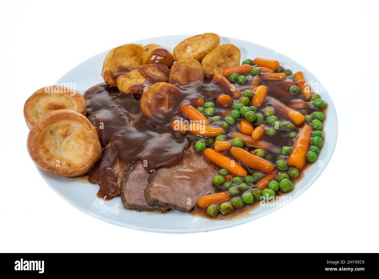 Cena di manzo arrosto con sugo di carne con piselli, carote, patate arrosto e budini dello Yorkshire - sfondo bianco Foto Stock