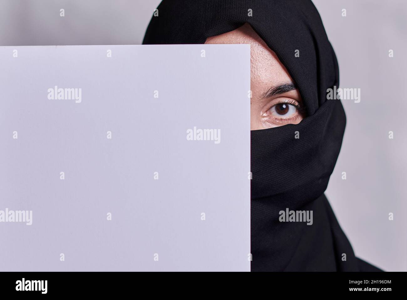 Giovani donne musulmane con occhi espressivi che ricoprono parte del suo volto con carta bianca. Ragazza musulmana in tradizionale hijab o nikab vestire che la copre Foto Stock