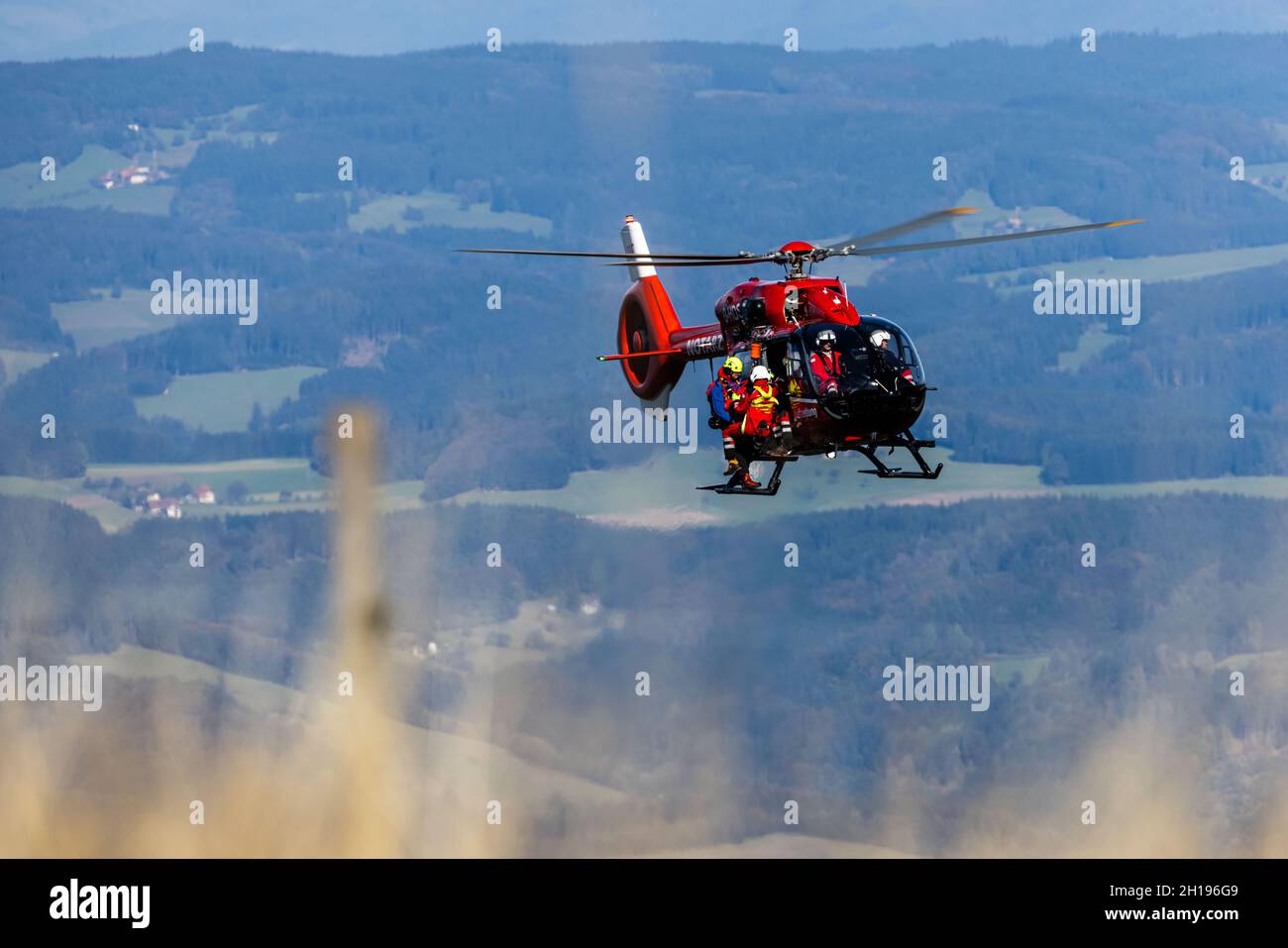 15 ottobre 2021, Baden-Wuerttemberg, Waldkirch: Un membro ciascuno del Bergwacht e del DRF Luftrettung si trova sulle piste di un elicottero di salvataggio, mentre la Foresta Nera può essere visto in background. Durante l'addestramento del verricello, l'equipaggio della stazione di Friburgo della DRF Luftrettung (cartello di chiamata Christoph 54) pratica le operazioni con il verricello sotto un elicottero insieme al Black Forest Mountain Rescue Service. Questo verricello può essere utilizzato per salvare i pazienti da terreni impraticabili, nonché per trasportare medici e paramedici in regioni difficili da raggiungere. Foto: Philipp von Ditfurth/dpa Foto Stock